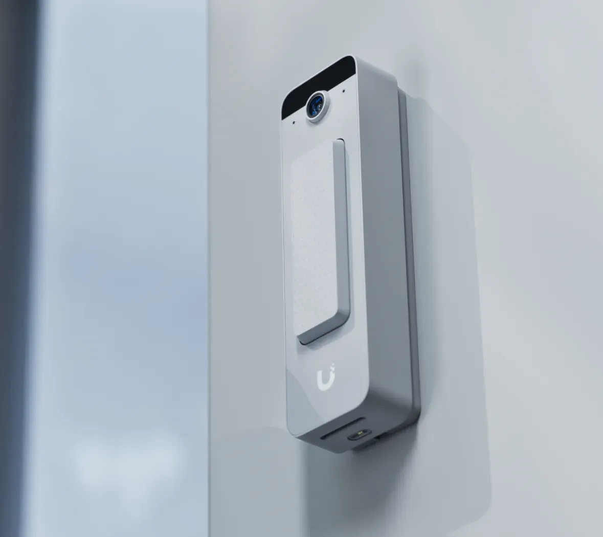 A doorbell on the wall beside a door, seen from the side so its depth and lens both read