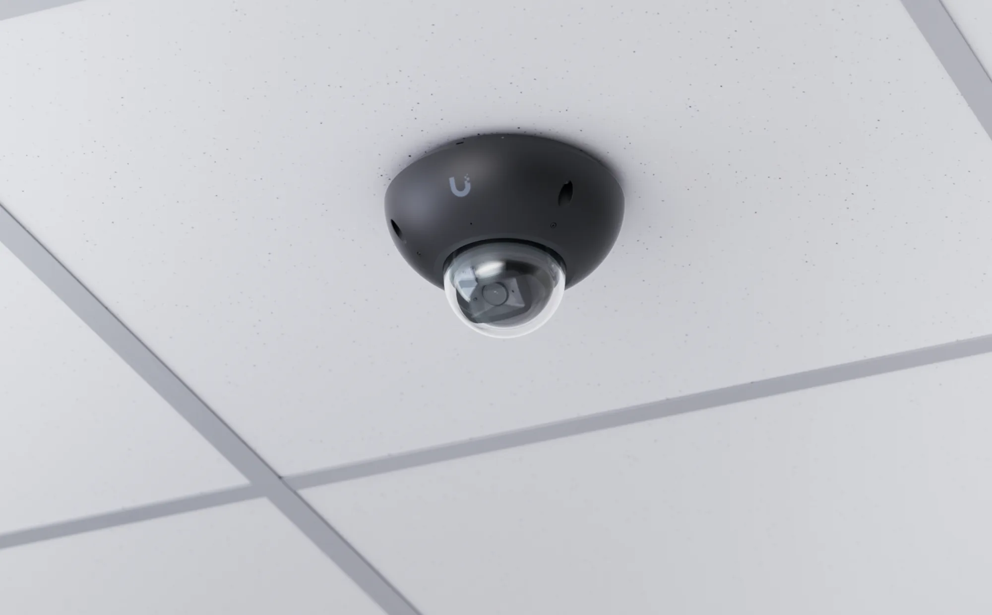 A dome camera on a suspended tile ceiling indoors, seen from below with the lens visible in its clear bubble