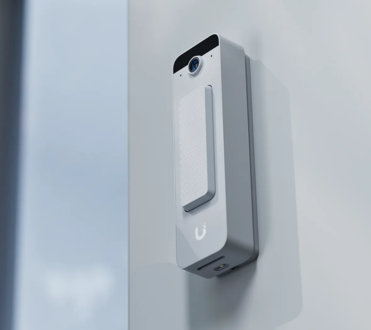 A doorbell on the wall beside a door, seen from the side so its depth and lens both read